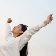 A person stretching their arms up against a bright sky