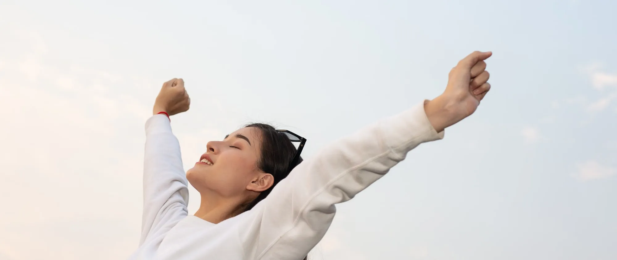 A person stretching their arms upward against a bright sky
